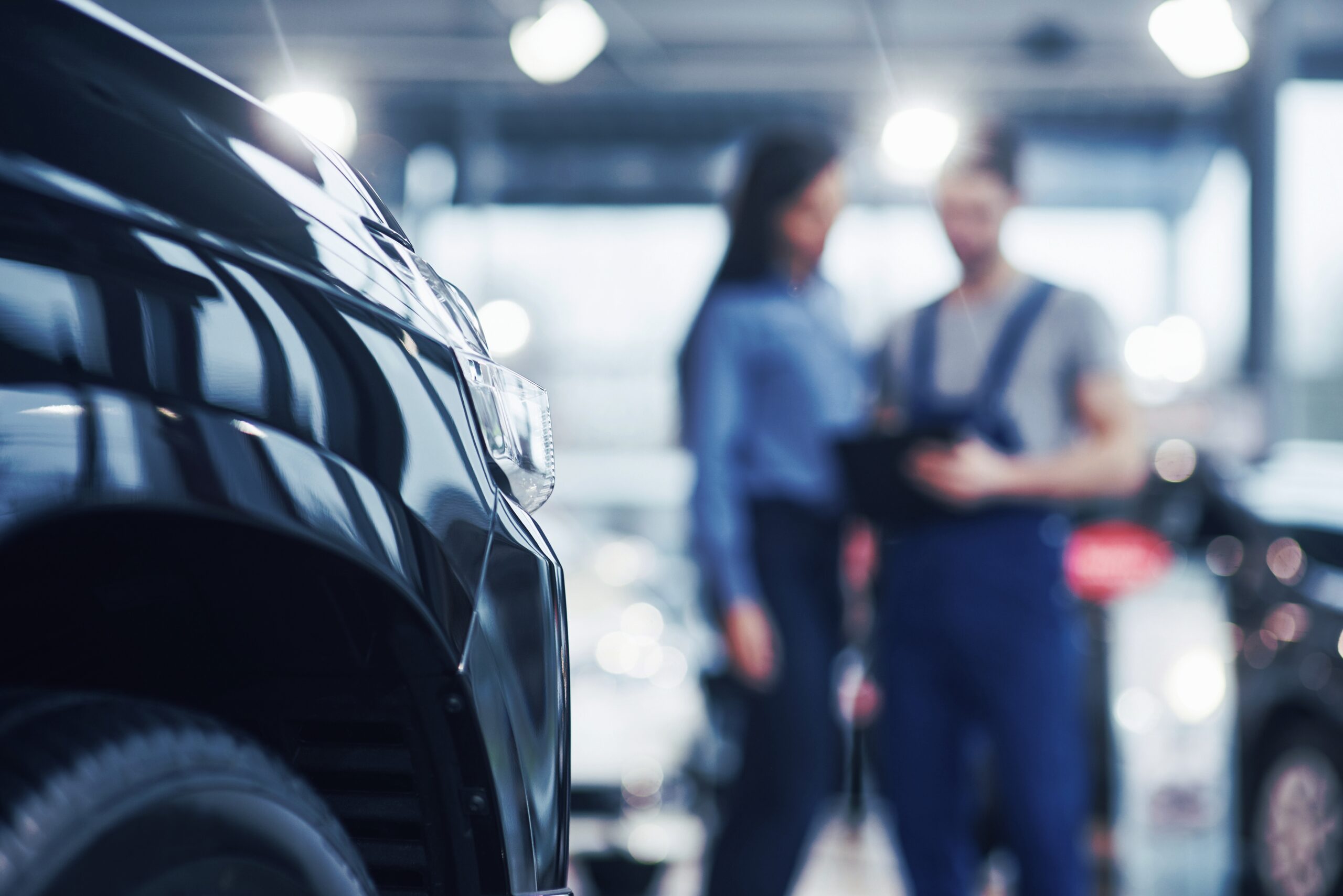 Beautiful young woman is talking to handsome car mechanic while repair a car in dealership